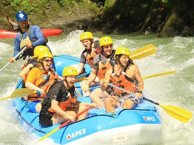 Group of people whitewater rafting down a rapid in a blue raft.
