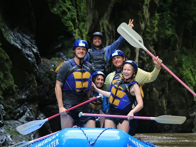 Four smiling rafters holding paddles on a blue boat on the Pacuare River.