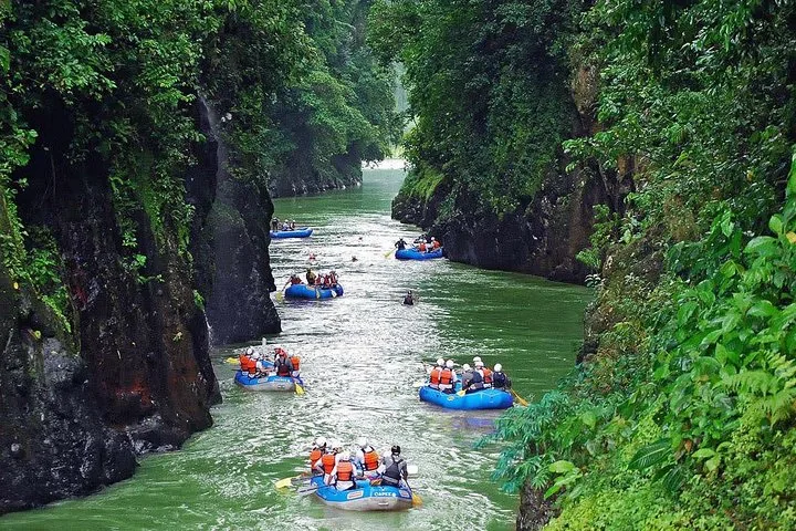 Plusieurs rafts bleus avec des touristes pagayant sur une rivière verte à l'intérieur d'un canyon
