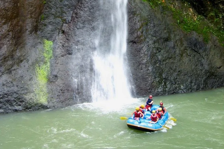 Touristes dans un raft pagayant près d'une cascade pittoresque se jetant d'une falaise